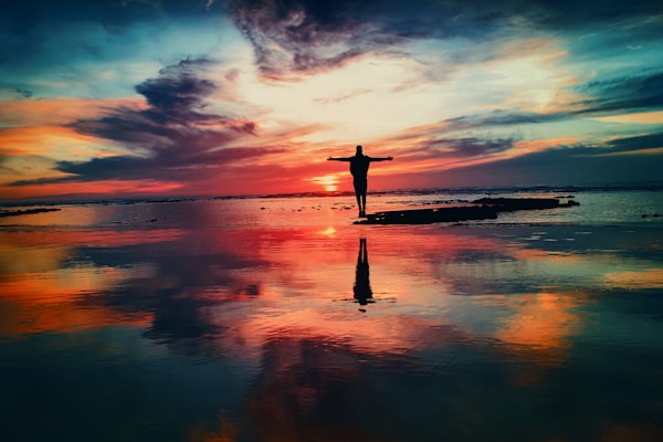 Person standing in water, with their arms spread under a sunrise.