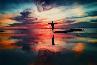 silhouette of person standing on rock surrounded by body of water passionate teams background