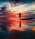 silhouette of person standing on rock surrounded by body of water