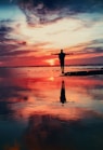 silhouette of person standing on rock surrounded by body of water