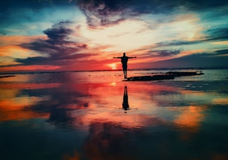 silhouette of person standing on rock surrounded by body of water