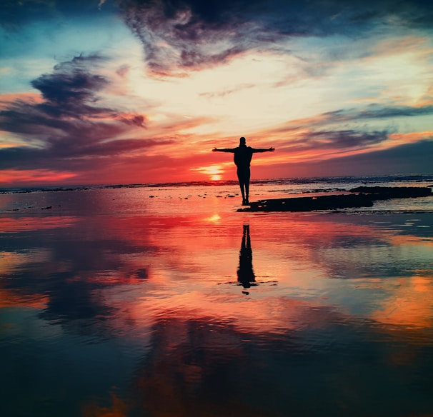 silhouette of person standing on rock surrounded by body of water