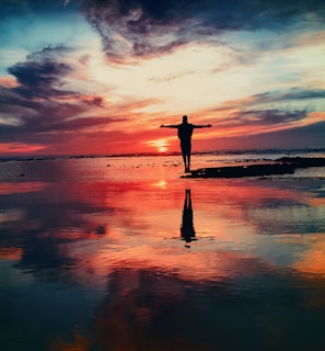 silhouette of person standing on rock surrounded by body of water