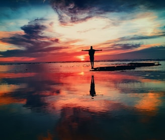 silhouette of person standing on rock surrounded by body of water