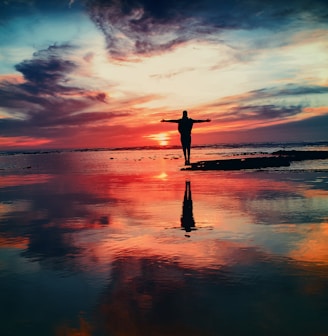 silhouette of person standing on rock surrounded by body of water