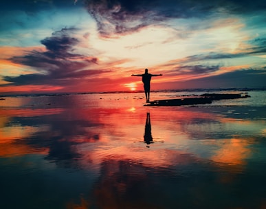 silhouette of person standing on rock surrounded by body of water