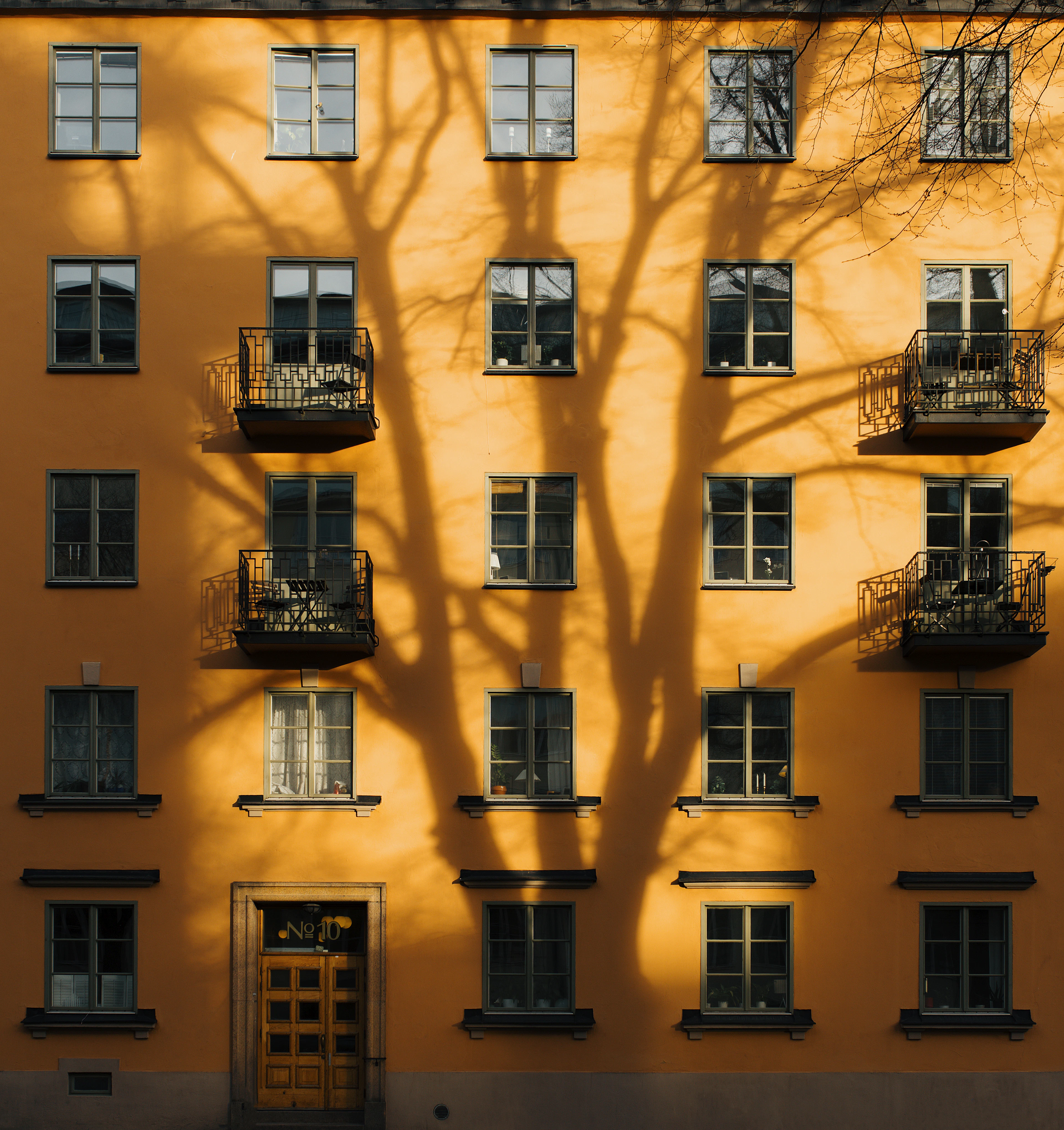 Orange flerbostadshus med skuggor av ett träd på fasaden