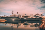 Dramatic sunset view of an aircraft carrier with planes lined up on deck, ready for takeoff.