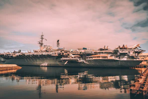 Dramatic sunset view of an aircraft carrier with planes lined up on deck, ready for takeoff.