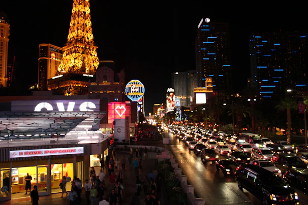 The shuttle van parked in front of the iconic Las Vegas Strip at night, glowing with neon lights.