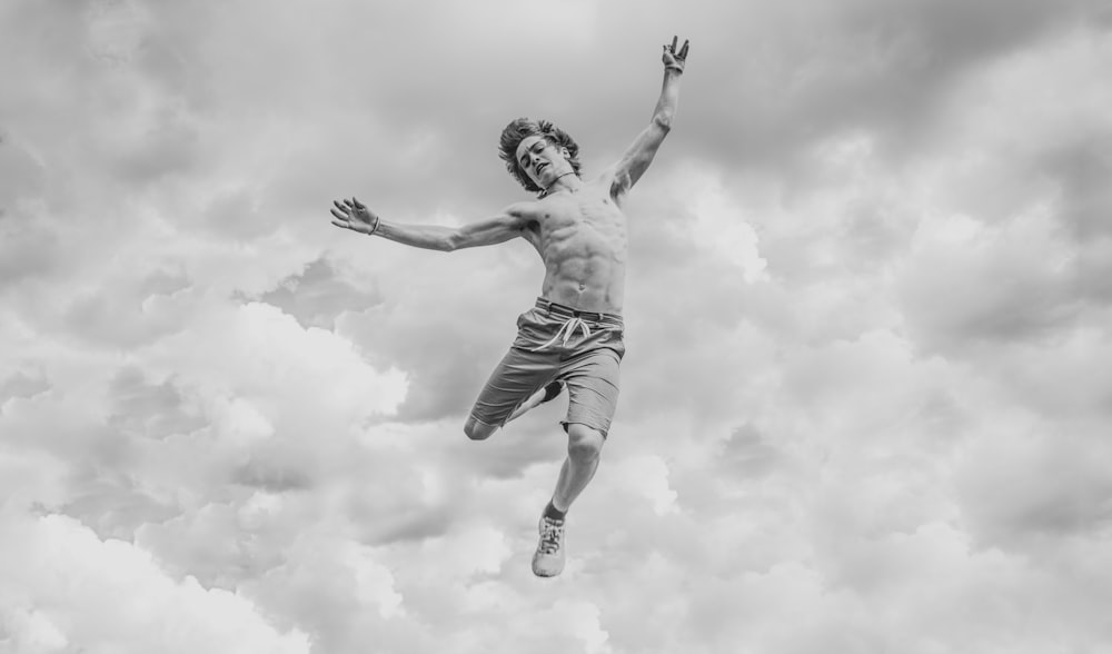foto em tons de cinza de pessoa pulando com vista para nuvens