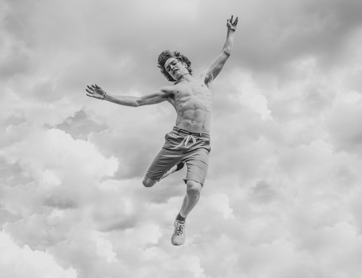 grayscale photo of person jumping overlooking clouds