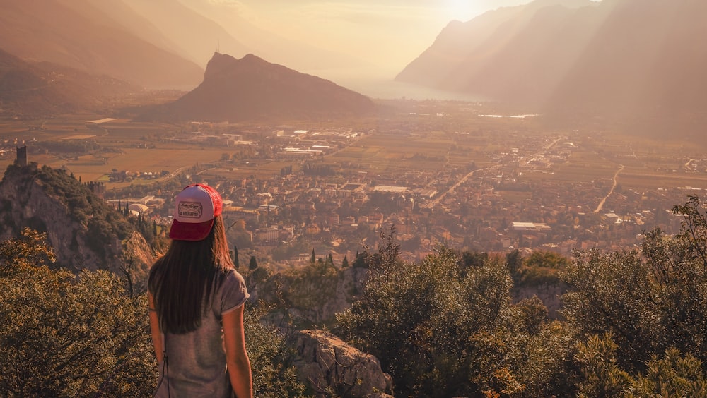 Mujer con camisa gris mirando hacia la ciudad cerca de la montaña durante el día