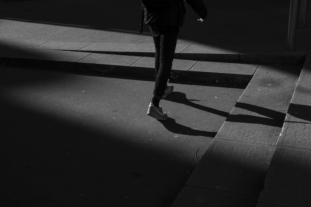 person wearing black pants and white shoes walking near gray concrete stairs