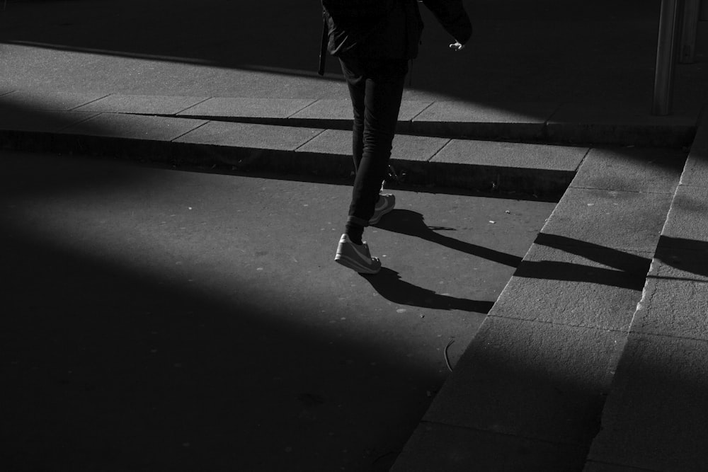 灰色のコンクリートの階段の近くを歩く黒いズボンと白い靴を履いた人