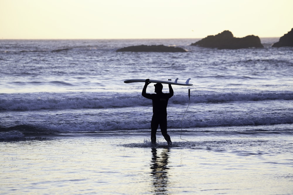 Silueta de hombre sosteniendo tabla de surf en la orilla del mar durante el día