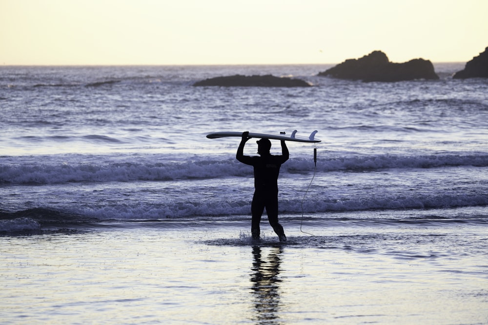 Silhouette di un uomo che tiene una tavola da surf in riva al mare durante il giorno