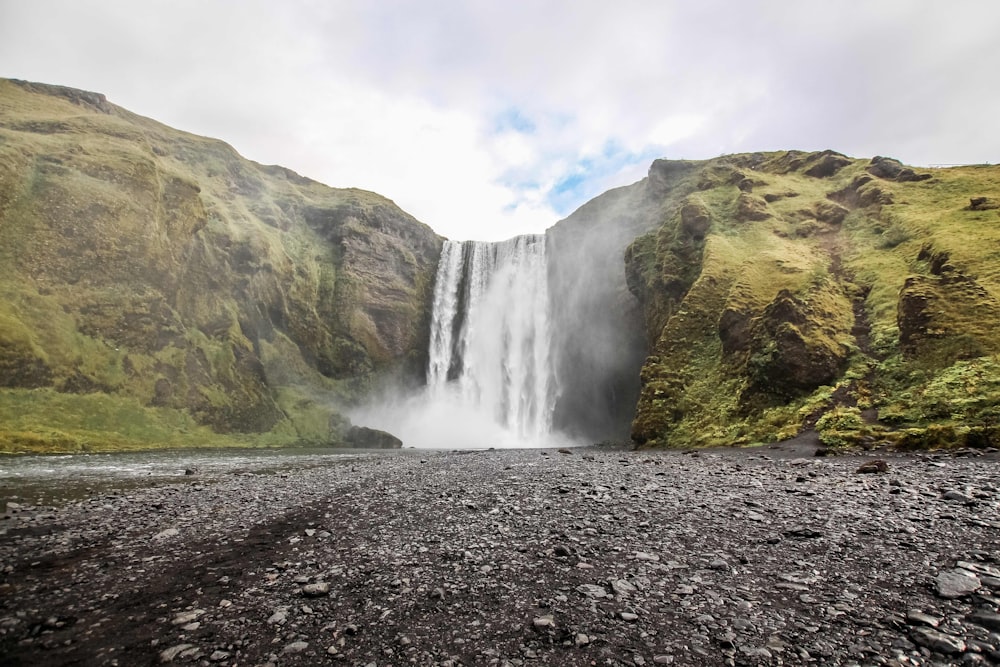 photo of waterfall near mountain under blue sky at daytime