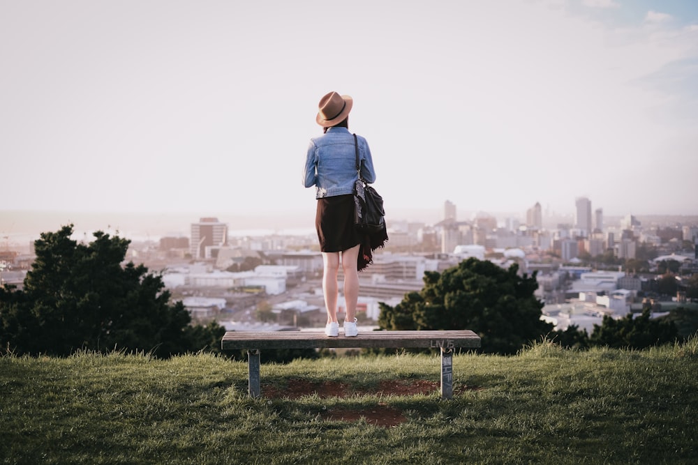 woman standing on bench facing city skyline during daytime