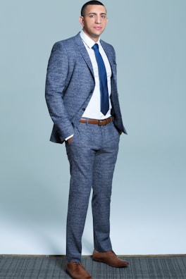 A sharp male model wearing a tailored navy blue suit with a crisp white shirt and patterned tie.