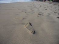 A serene beach at dawn with footprints leading toward the calm ocean waves.