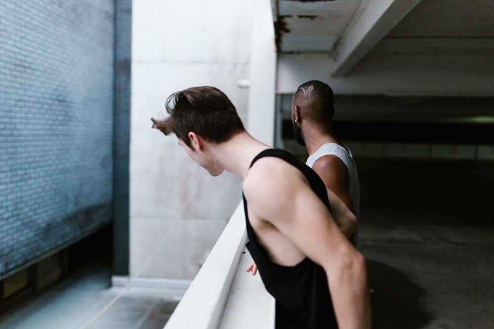 two men in tank tops standing near railing