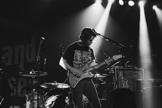 greyscale photo of man playing electric guitar on stage