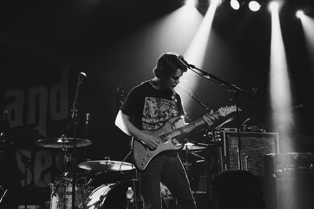 greyscale photo of man playing electric guitar on stage
