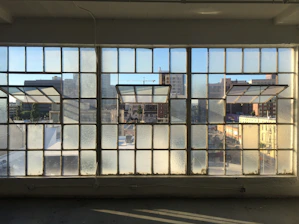 Large glass window with black frame overlooking a cityscape on a sunny day.