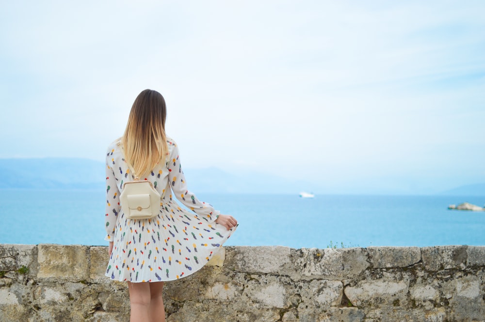 woman in white dress looking at body of water