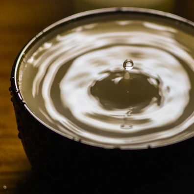 An artistic shot of foundation drops falling onto a reflective surface creating ripples.