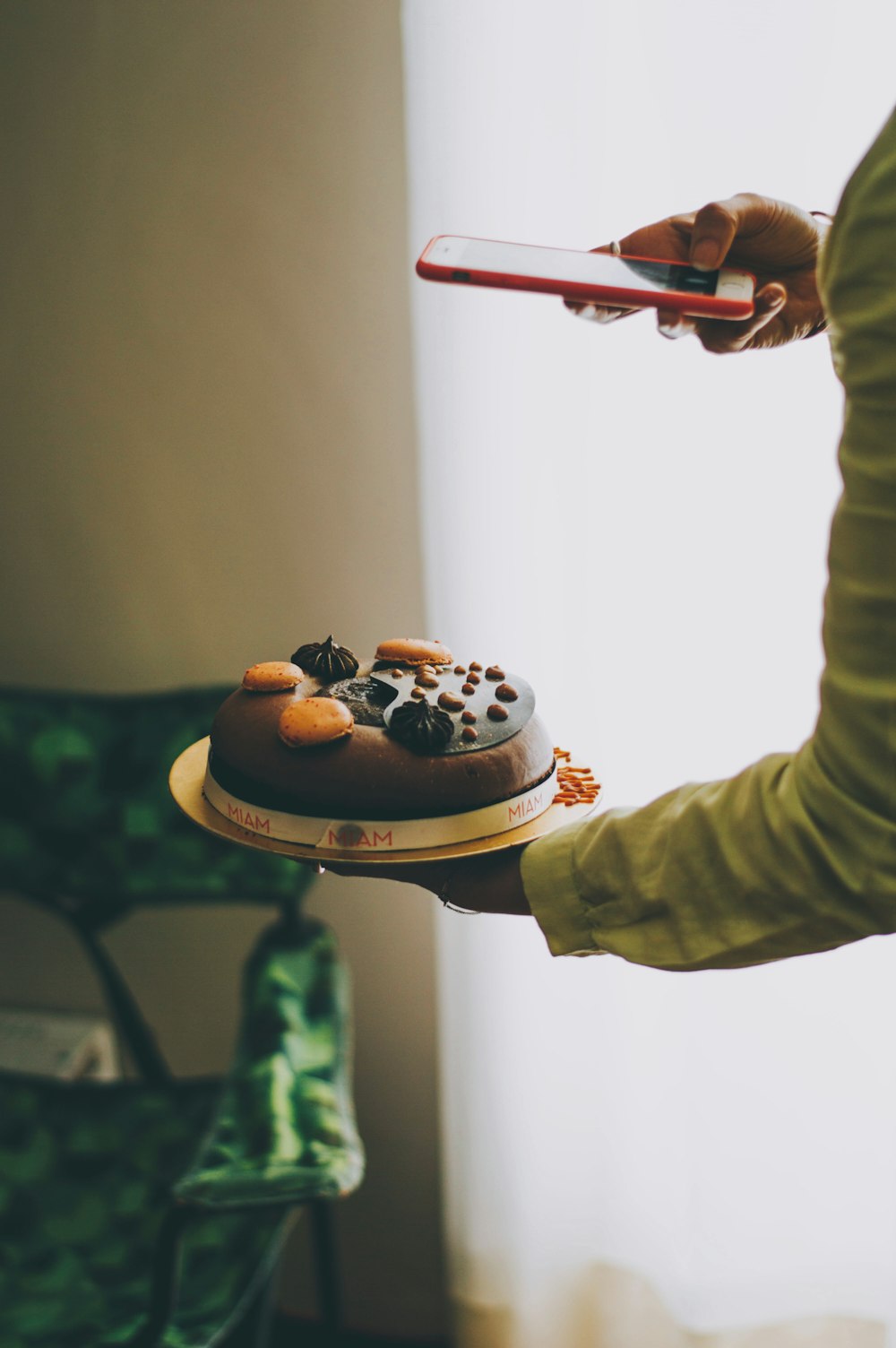 person holding iPhone taking photo of cake near curtains