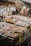 An outdoor market stall featuring a variety of packaged goods and seafood. The packages are displayed on tables made of stacked crates under hanging light bulbs. Surrounding the display, there are cardboard boxes and handwritten labels. The setting has a rustic and bustling market atmosphere.