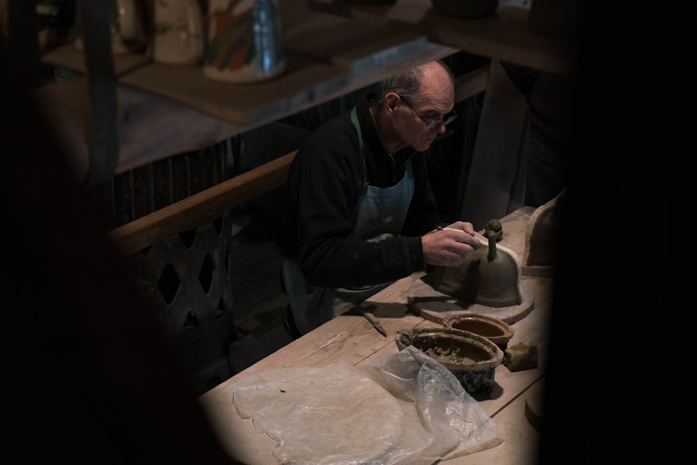 man in black long-sleeved shirt and blue apron working on gray pot on table