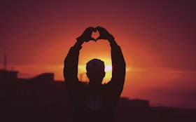 Sombra de um homem com braços estendidos e mãos formando o símbolo de um coração