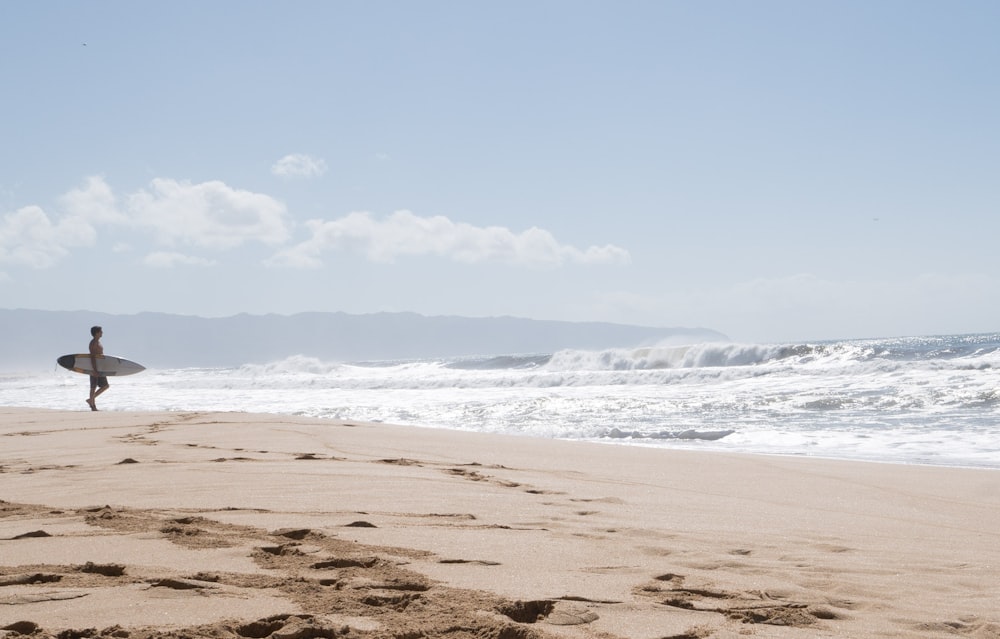 person holding white surfboard standing on seashore during daytime