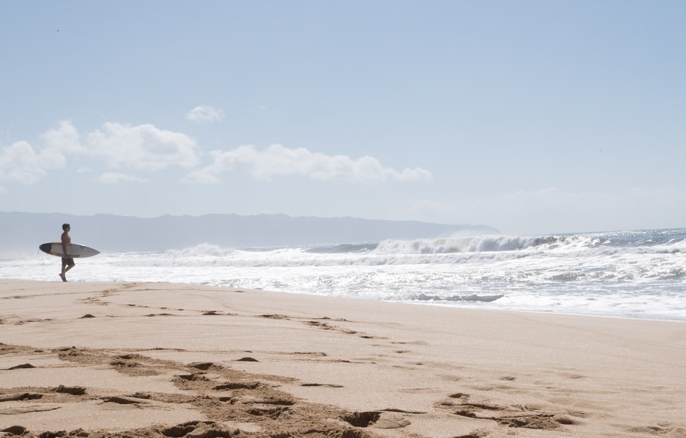 pessoa segurando prancha de surf branca em pé na costa durante o dia