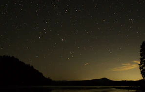 A serene night sky filled with bright stars and a glowing crescent moon over a calm landscape