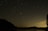 A vibrant night sky filled with stars and a glowing moon over a calm landscape.