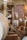 A rustic interior with wooden beams and brick walls. There are large wooden barrels and wicker baskets spread around the space. Various kitchen items like plates and mugs are visible in the background. A rope hangs from the structure above, adding to the traditional look.