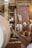 A rustic interior with wooden beams and brick walls. There are large wooden barrels and wicker baskets spread around the space. Various kitchen items like plates and mugs are visible in the background. A rope hangs from the structure above, adding to the traditional look.