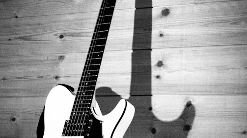 A sleek bass guitar leaning against a textured wooden wall, highlighting its glossy dark finish.