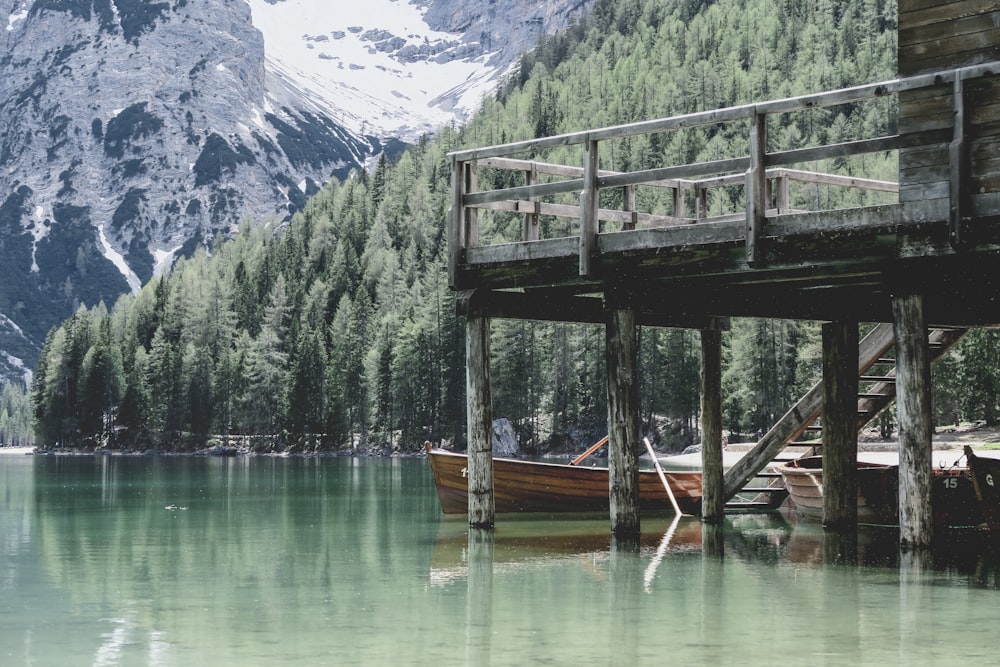 brown wooden boat on body of water near green trees and mountain during daytime