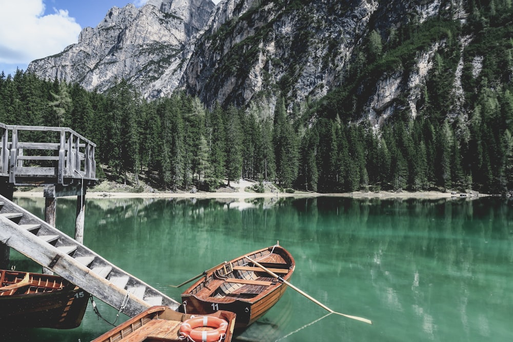 brown wooden boat on lake near green trees and mountain during daytime