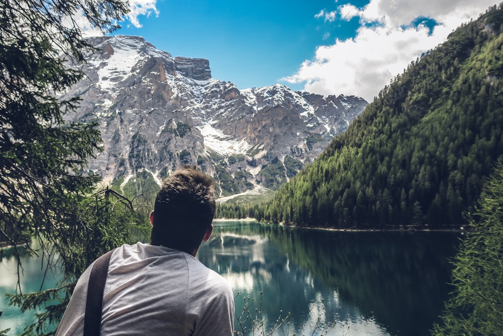 man in white shirt sitting on rock looking at lake and mountains during daytime