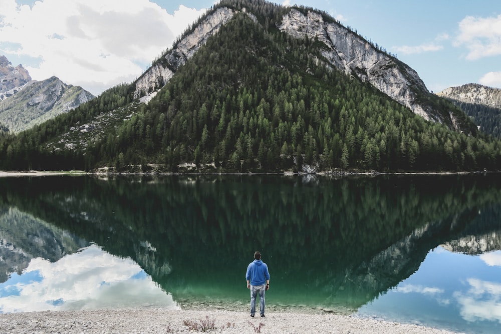 man standing nearby sea fronting green mountain