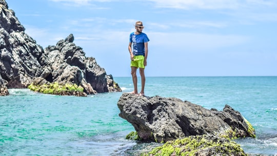 man in blue t-shirt standing on gray rock on see in Isla Margarita Venezuela