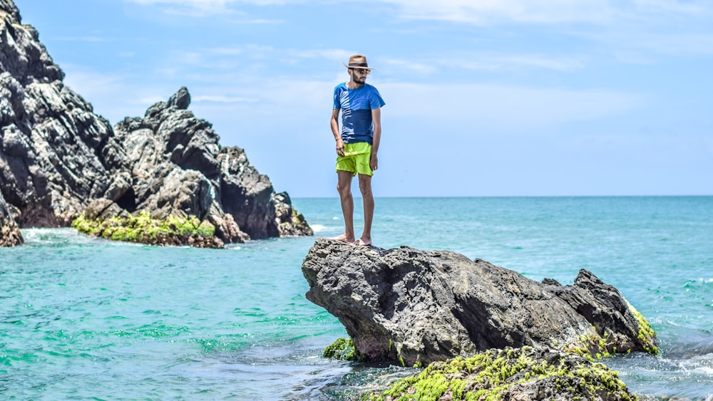 man in blue t-shirt standing on gray rock on see