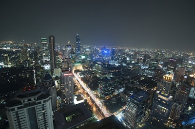 A cityscape at night with numerous skyscrapers and buildings illuminated by artificial lights. The skyline is densely packed, showcasing a vibrant urban environment with bright streetlights and visible traffic.