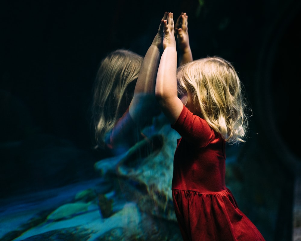 girl leaning on glass fish tank raising her two hands